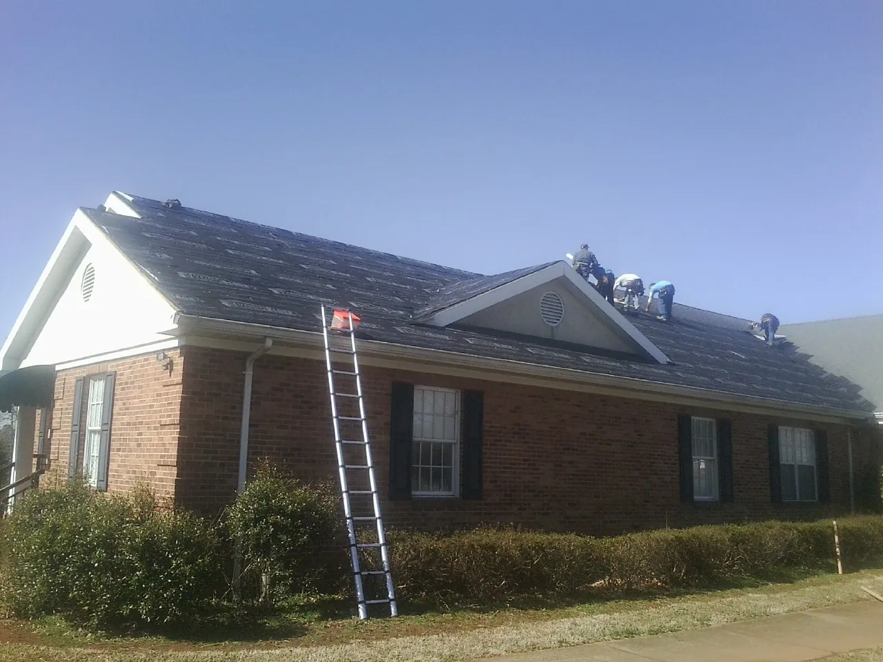 Crew tearing shingles off a brick ranch roof with a ladder set — Emergency Roof Repair work by our crew in Joice