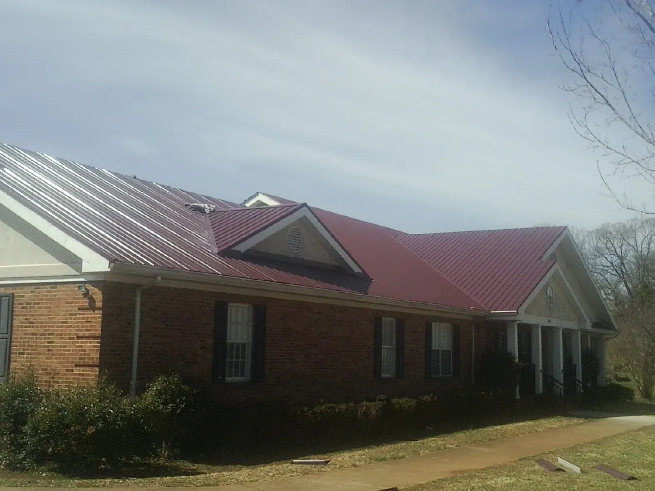 Red metal roof with gabled entries on a long brick building, from a Hail Damage Roof Repair job in Joice