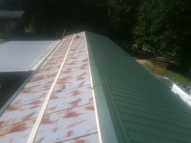 Old rusted panels beside newly installed green metal roofing — Wind Damage Roof Repair by Roofing Brothers in Joice