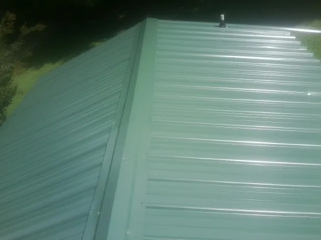 New green metal panels meeting at the ridge of a roof — Flat Roof Repair work by our crew in Joice