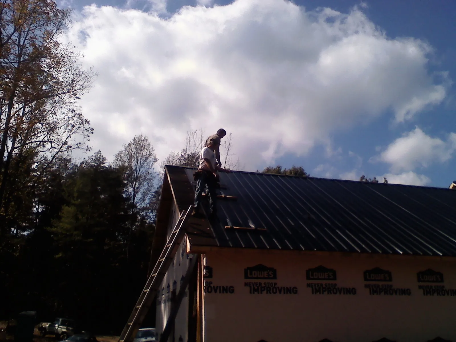 Roofer fastening dark metal panels high against a cloudy sky, from a Roof Inspection job in Joice