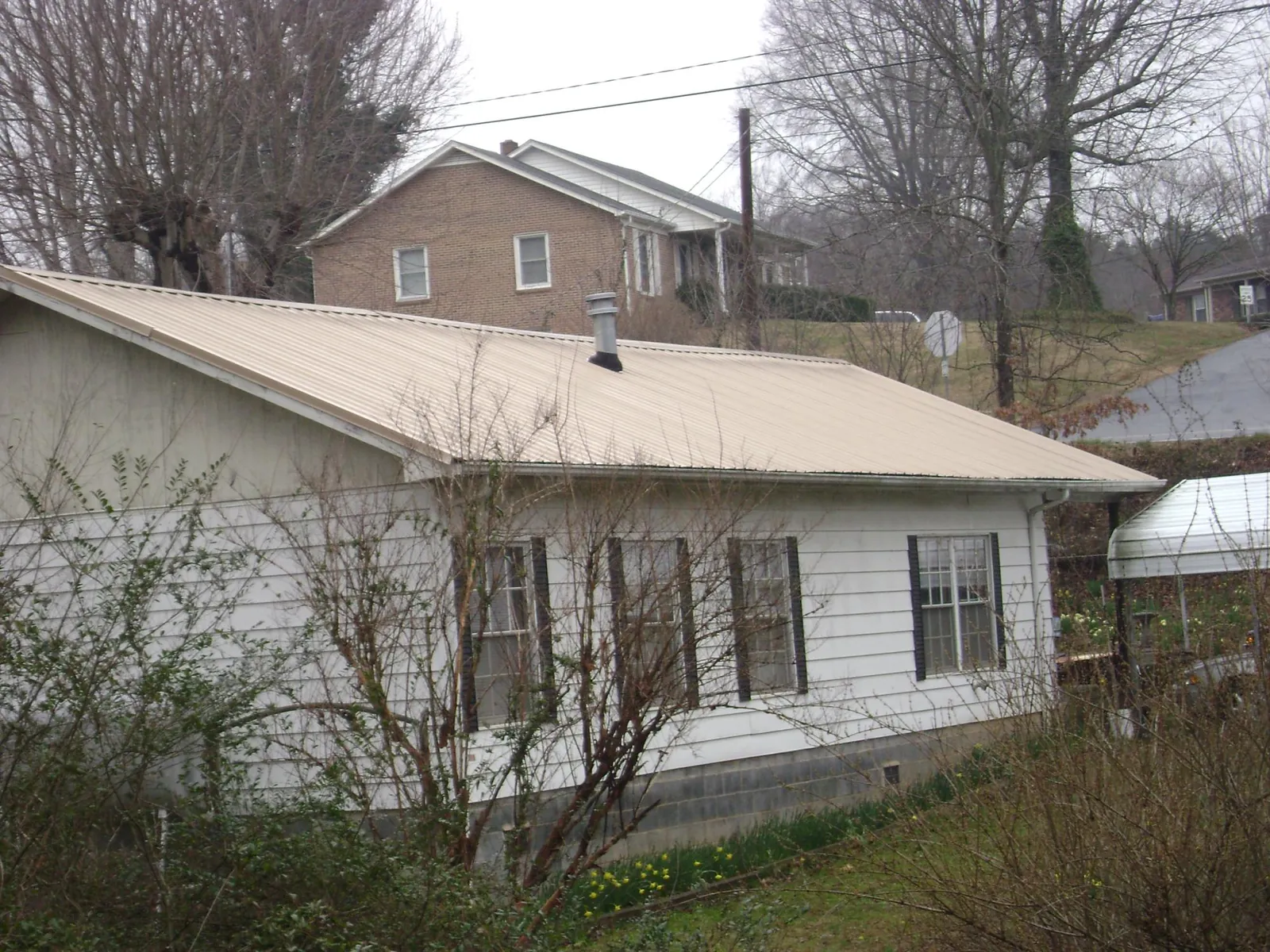 Tan metal roof on a white sided house set into a hillside — Commercial Roofing by Roofing Brothers in Joice