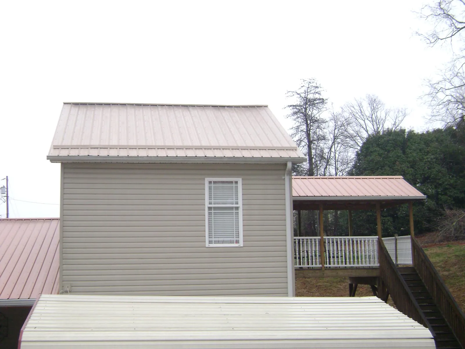 Tan metal roofs on a two story addition and attached porch, from a Roof Replacement job in Joice